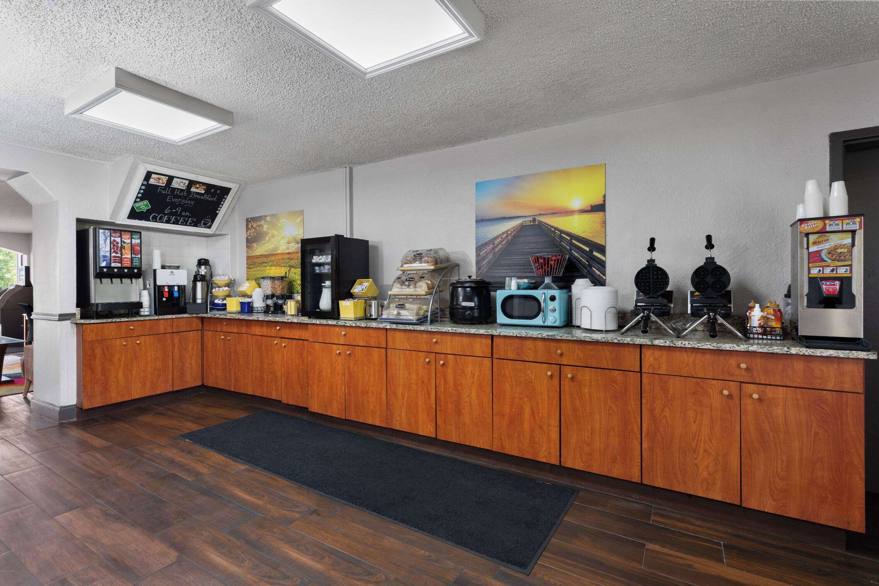 Una cocina moderna con armarios de madera, un espacio para café, microondas y un cuadro grande con un atardecer sobre un muelle.