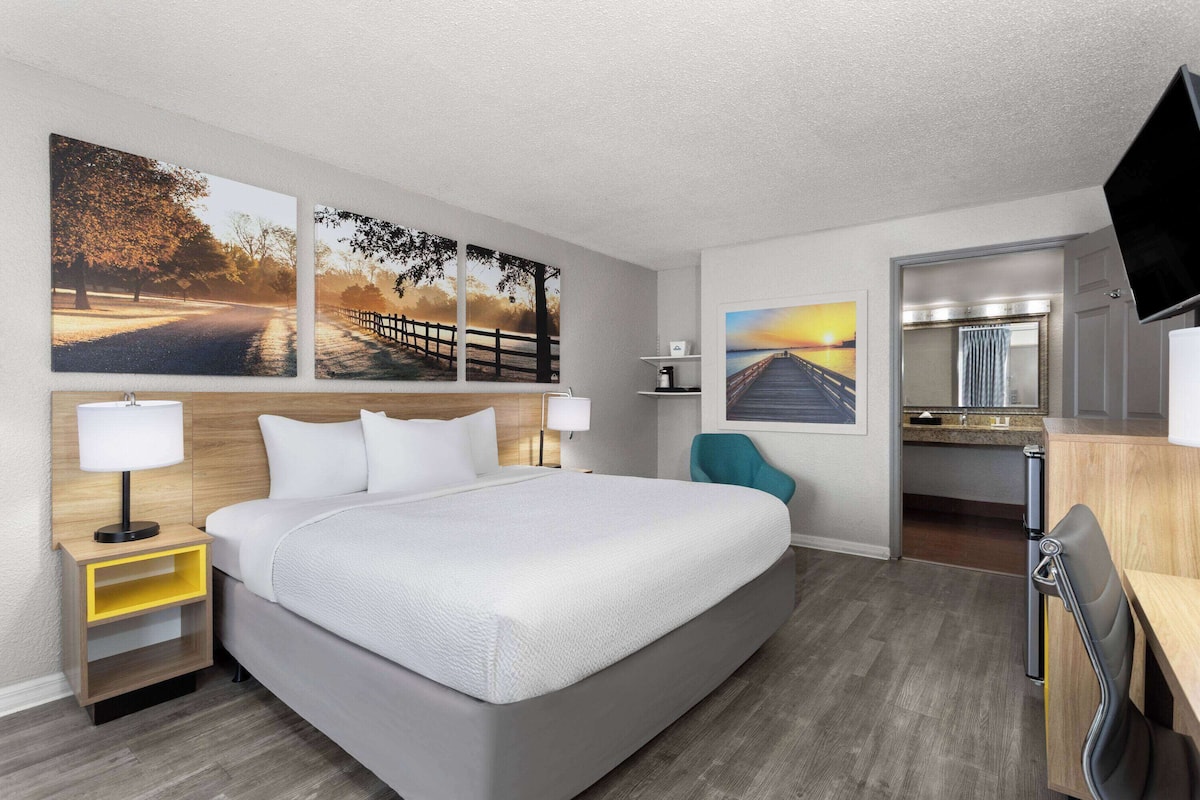 A hotel room with a large bed, a desk with a chair, a TV, and artwork on the walls.