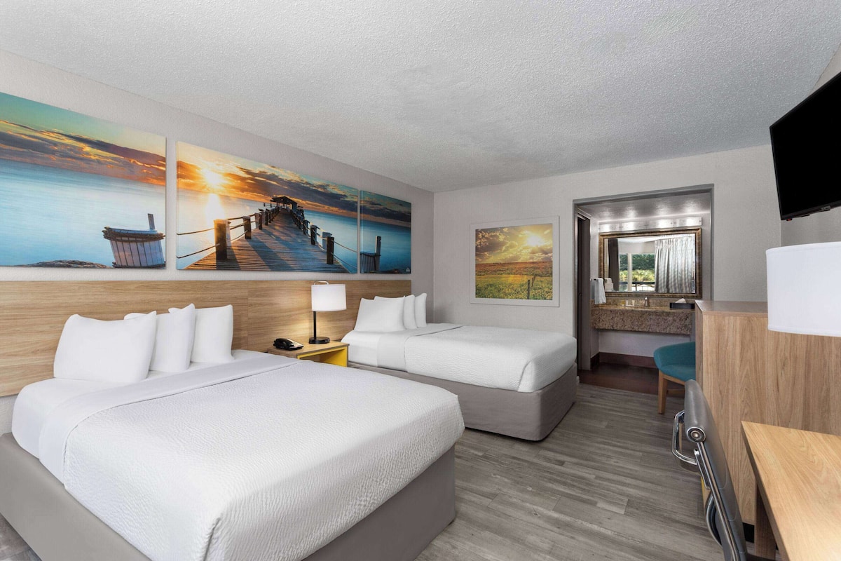 A hotel room with two beds, a desk, a chair, and artwork on the walls.