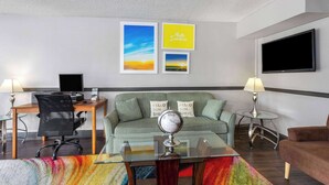 A hotel room with a desk, a couch, a TV, and two lamps. - Days Inn by Wyndham Wildwood I-75 (Wildwood)