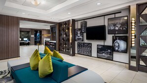 A modern hotel lobby with a teal sofa, a reception desk, and a wall with framed pictures and a TV. - Hilton Garden Inn Los Angeles/Hollywood (Los Angeles)