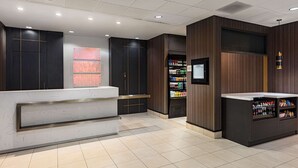 A modern reception area with a marble counter, wooden paneling, and a beverage vending machine. - Hilton Garden Inn Los Angeles/Hollywood (Los Angeles)