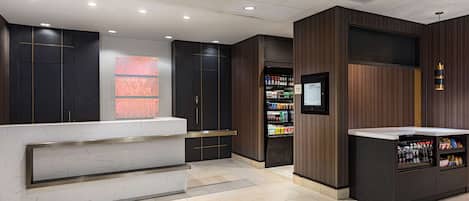 A modern reception area with a marble counter, wooden paneling, and a beverage vending machine.