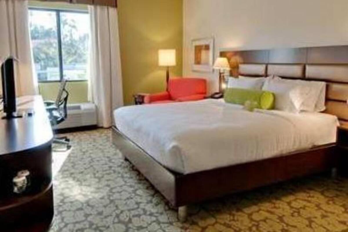 A hotel room with a bed, a desk, a chair, a lamp, and a window.