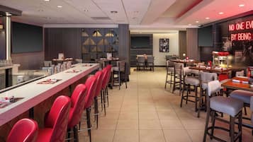 A modern restaurant with a long counter, red bar stools, and a neon sign.