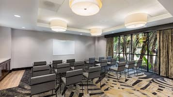 Une salle de conférence avec des rangées de chaises, un écran de projection et de grandes fenêtres équipées de rideaux.
