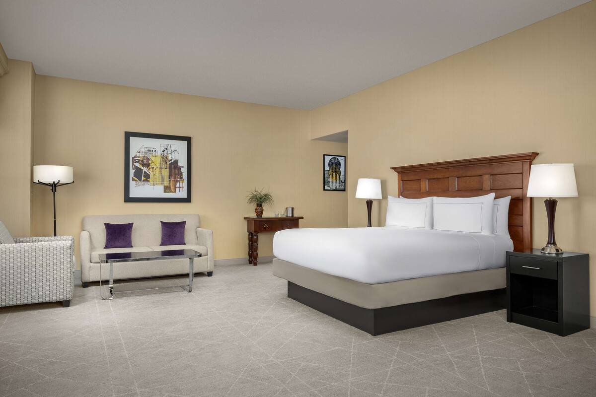Une chambre d’hôtel avec un lit, un canapé, une table de chevet et une lampe.