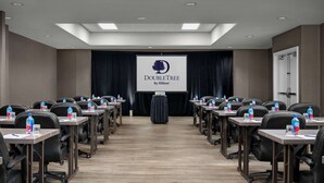 Une salle de conférence équipée d’un écran de présentation, de rangées de tables avec des chaises et de bouteilles d’eau sur chaque table.