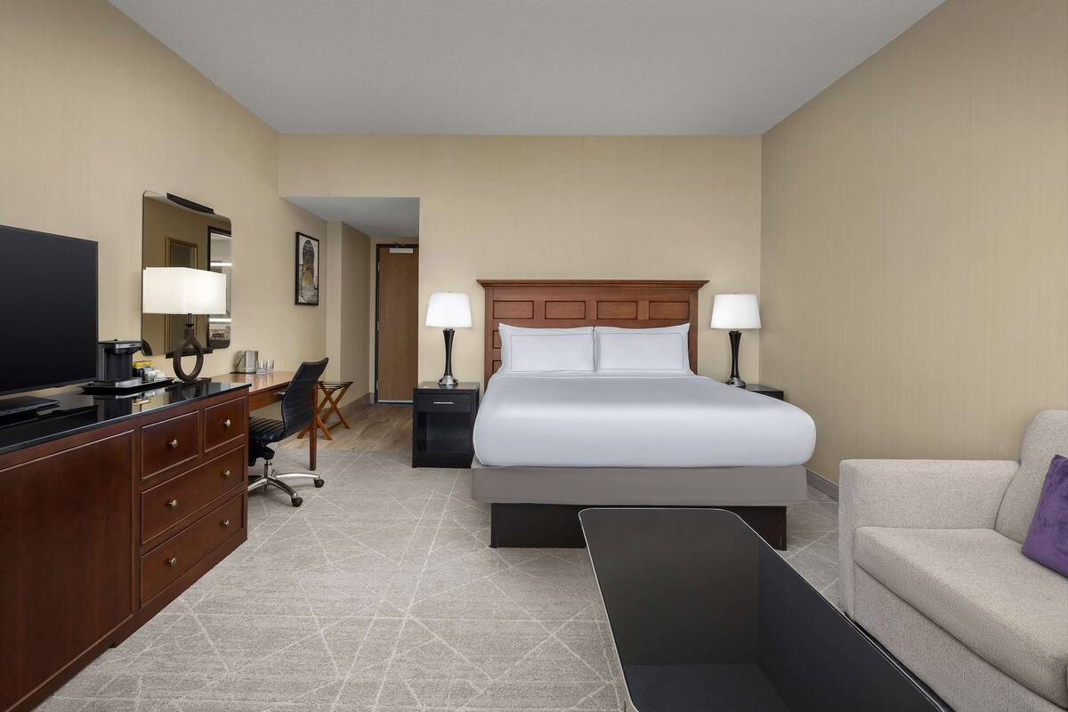 Une chambre d’hôtel avec un lit, un bureau avec un ordinateur, une télévision et un canapé.