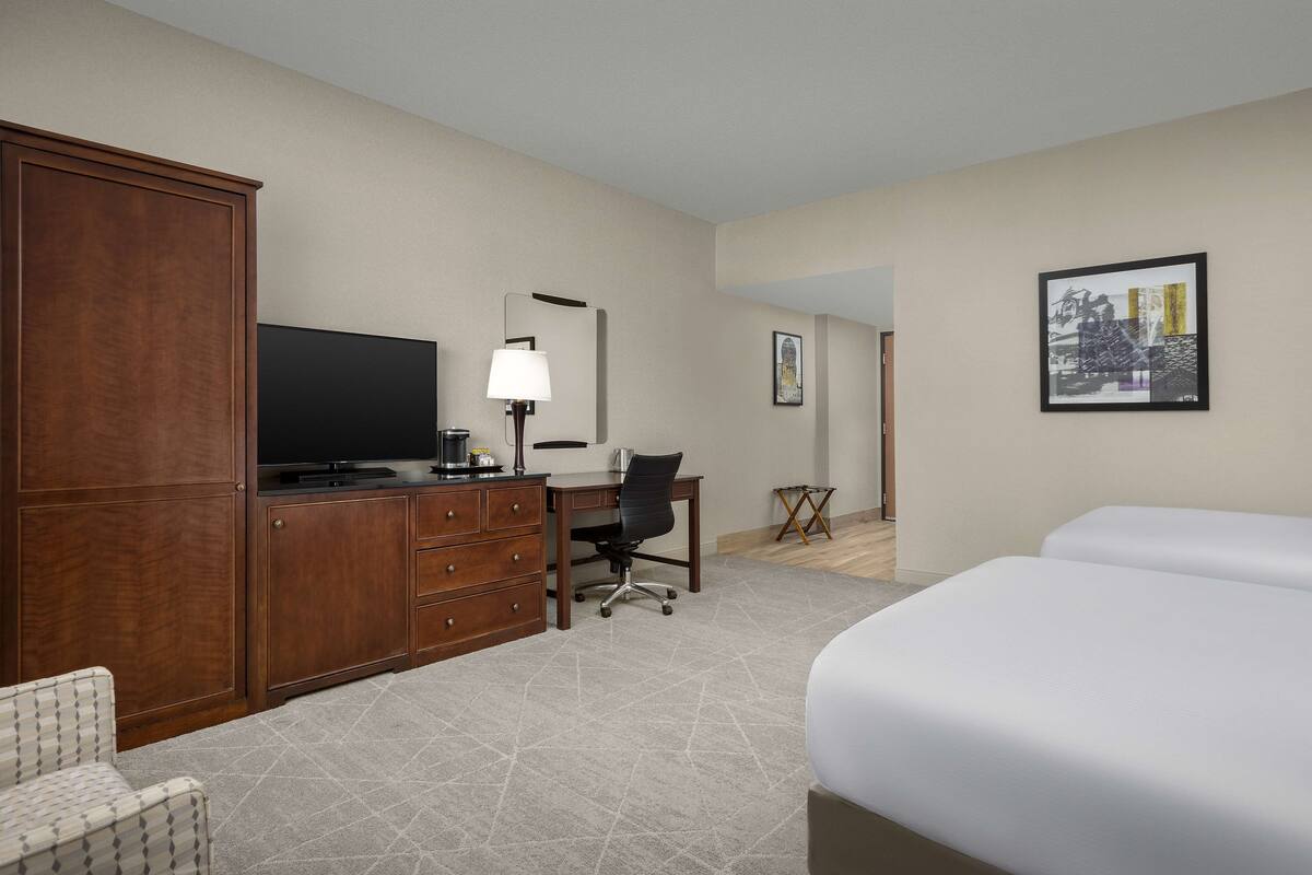 Une chambre d’hôtel avec un grand lit, un bureau avec une chaise, une télévision, une armoire et un tableau encadré au mur.