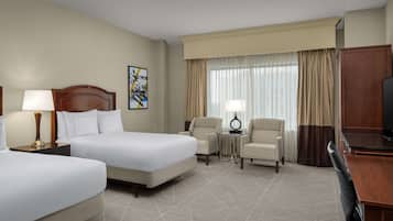 Habitación de hotel con dos camas, un escritorio, una silla, un televisor y una ventana con cortinas.