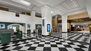 Un hall d’entrée avec un sol à carreaux, des sièges verts, un comptoir de réception et une enseigne indiquant « BC Suites & Towne ».