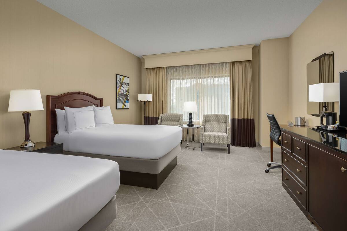 Une chambre d’hôtel avec deux lits, un bureau, une chaise, une commode et un téléviseur.