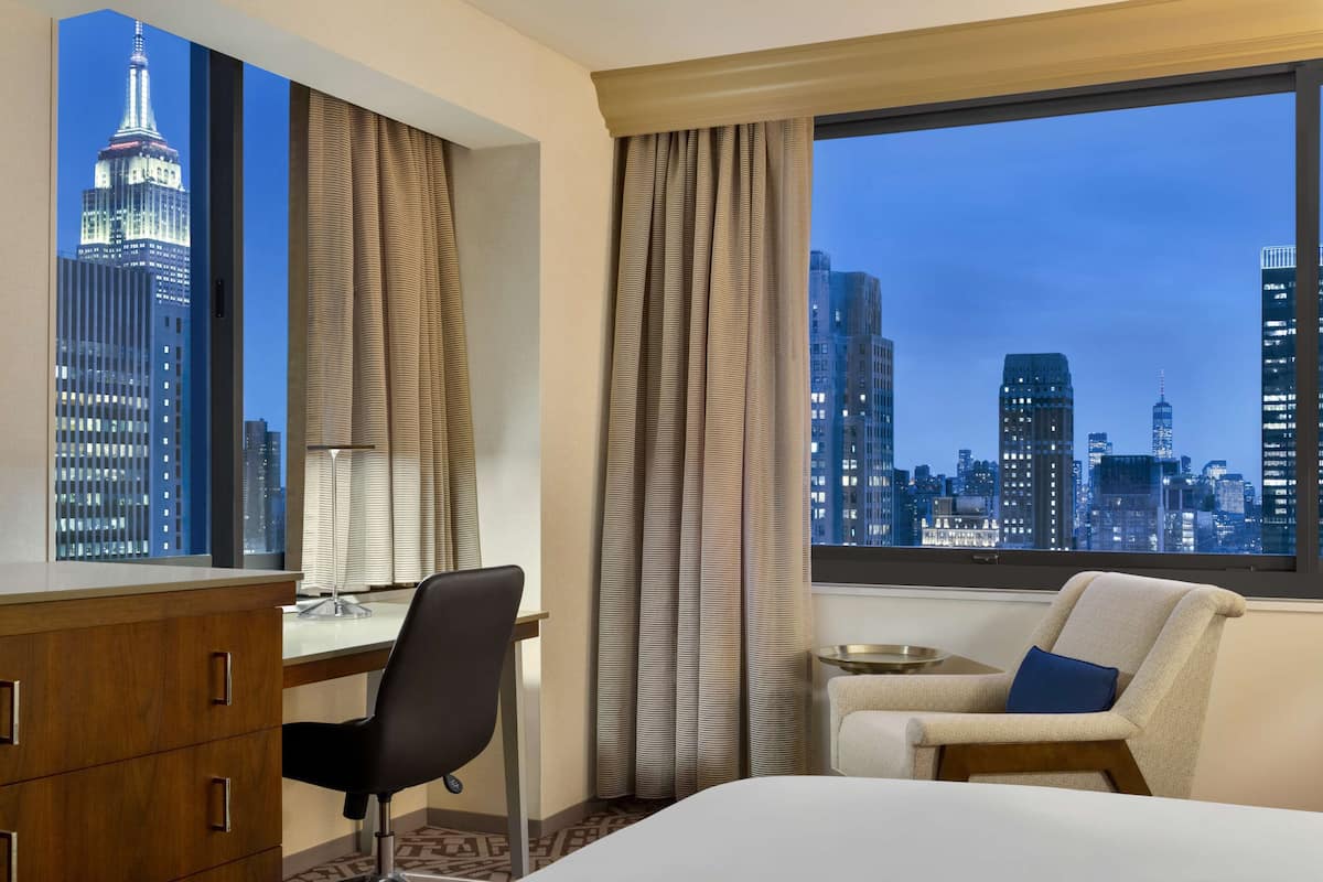 Une chambre d’hôtel avec un lit, un bureau, une chaise et une vue sur les toits de la ville.