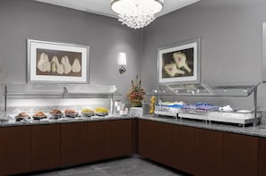 A buffet area with various food items, a chandelier, and framed artwork on the walls. - Hilton New York Times Square (New York)