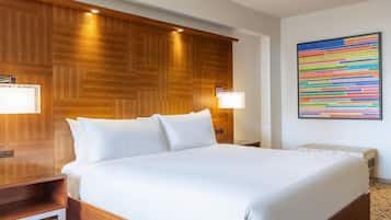 A hotel room with a wooden headboard, a large bed with white linens, two bedside lamps, and a wall-mounted information board.