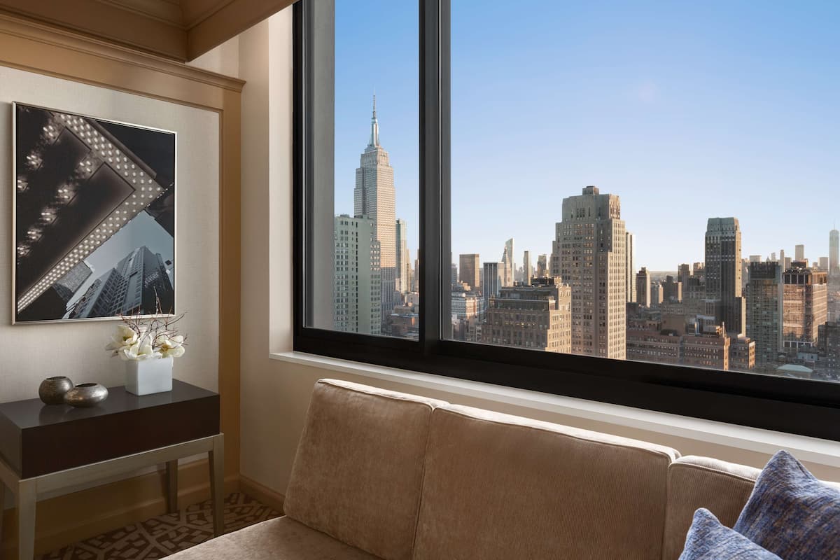 Une pièce dotée d’une grande fenêtre offrant une vue panoramique sur la ville, d’une console moderne agrémentée d’objets décoratifs et d’un coin salon confortable.