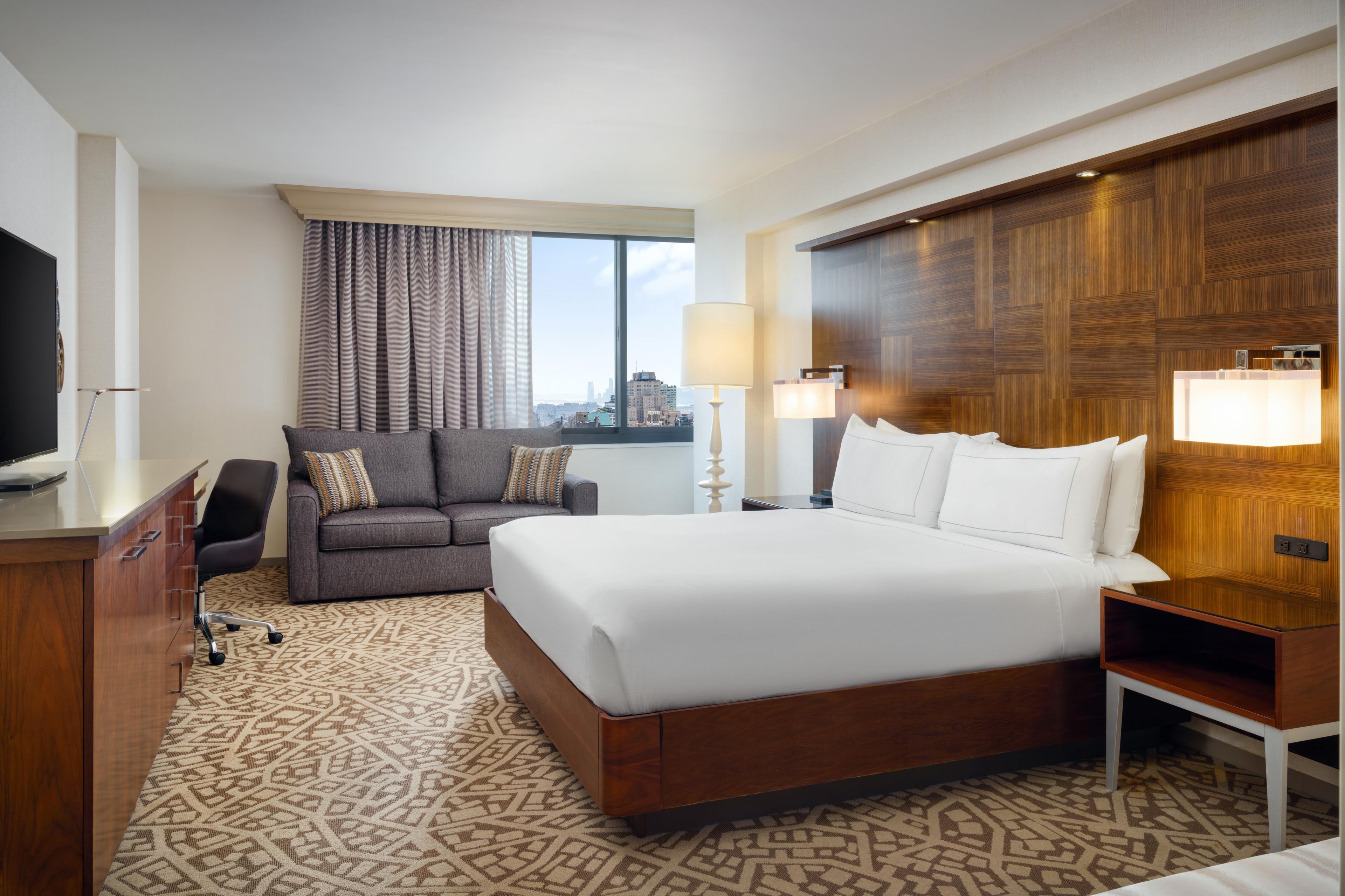 Una habitación de hotel con una cama grande, un sofá, un escritorio, un televisor y una ventana con cortinas.