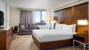 Una habitación de hotel con una cama grande, un sofá, un escritorio, un televisor y una ventana con cortinas.