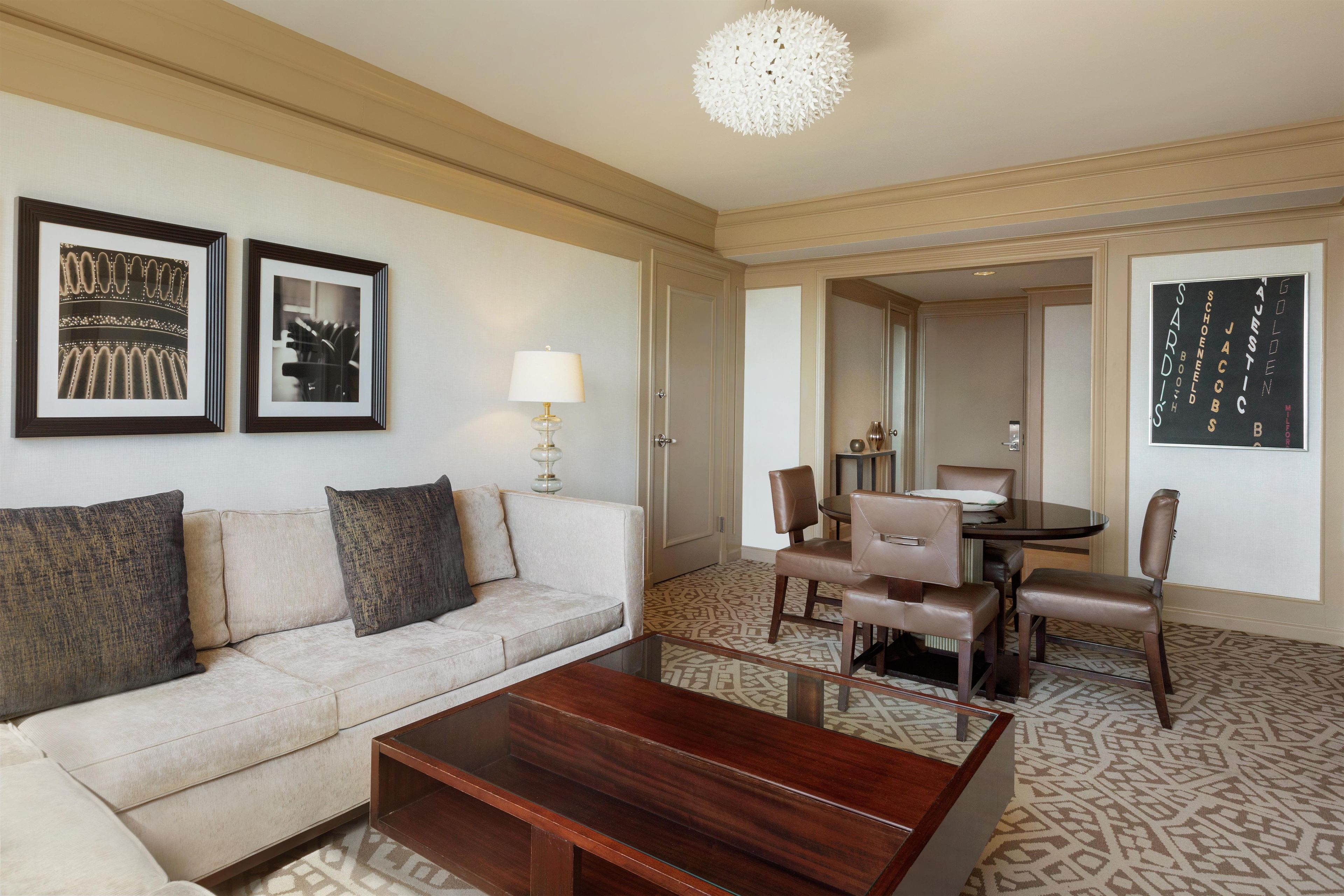 A hotel room with a sofa, a coffee table, a dining table with chairs, and framed pictures on the wall.