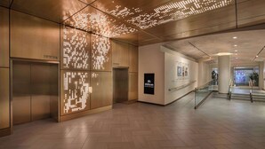 A modern hotel lobby with a digital art installation on the wall, a glass railing, and a sign indicating the hotel name. - Hilton New York Times Square (New York)