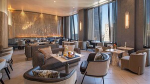 A spacious hotel lobby with modern furniture, a central seating area, and large windows offering city views. - Hilton New York Times Square (New York)