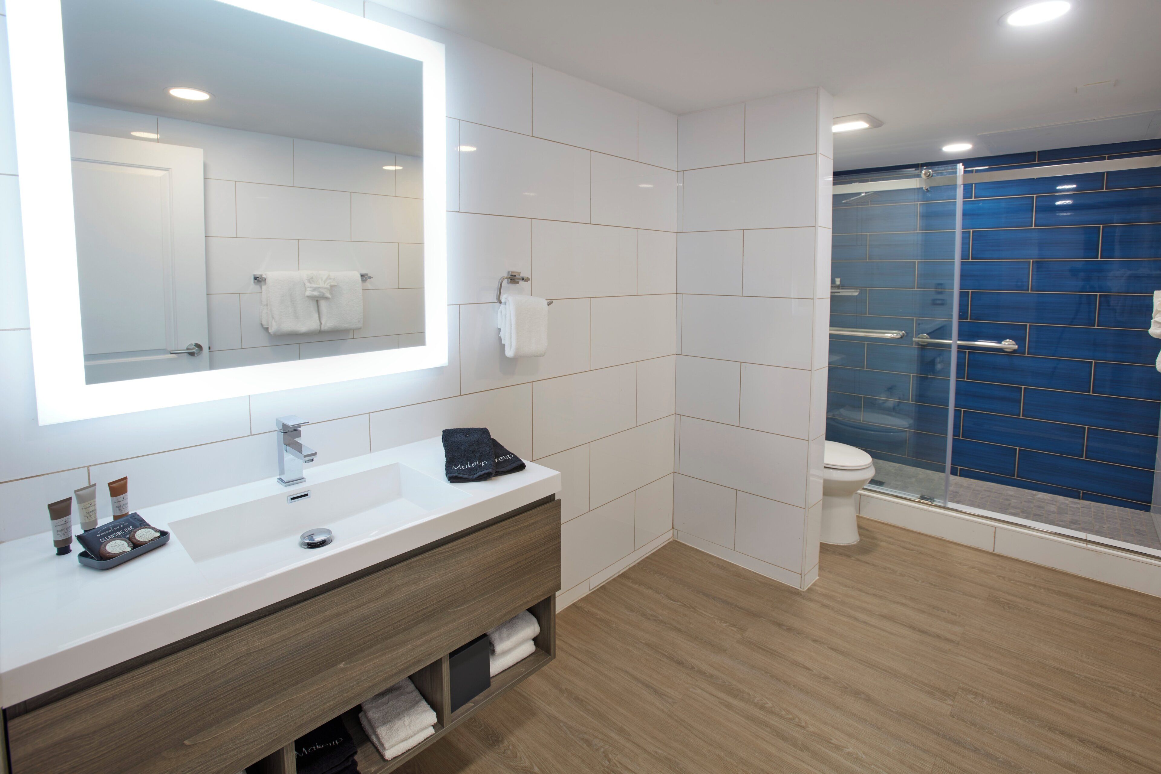 A modern bathroom with a white vanity, a large mirror, a glass shower enclosure, and a white toilet.