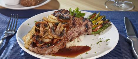 A plate of steak with mushrooms and a side of vegetables, accompanied by bread and a glass of wine on a table.