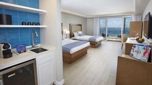 Una habitación de hotel con dos camas, una kitchenette, un amplio ventanal con vista al mar y un balcón.