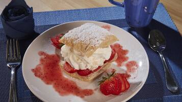 Une assiette à dessert avec une pâtisserie, de la crème fouettée et des fraises, le tout posé sur un set de table bleu.