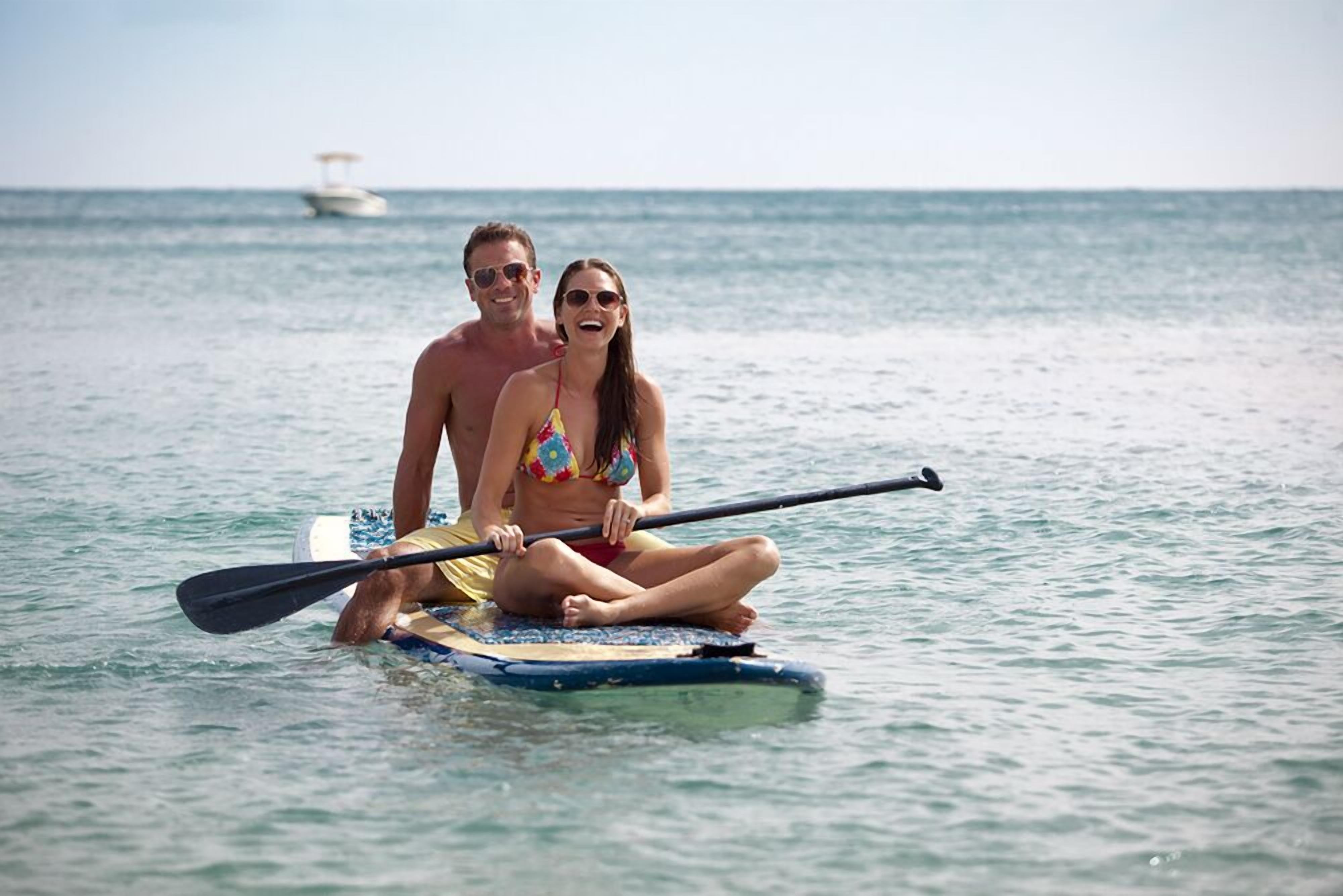 A couple on a paddleboard in calm waters with a boat in the background.