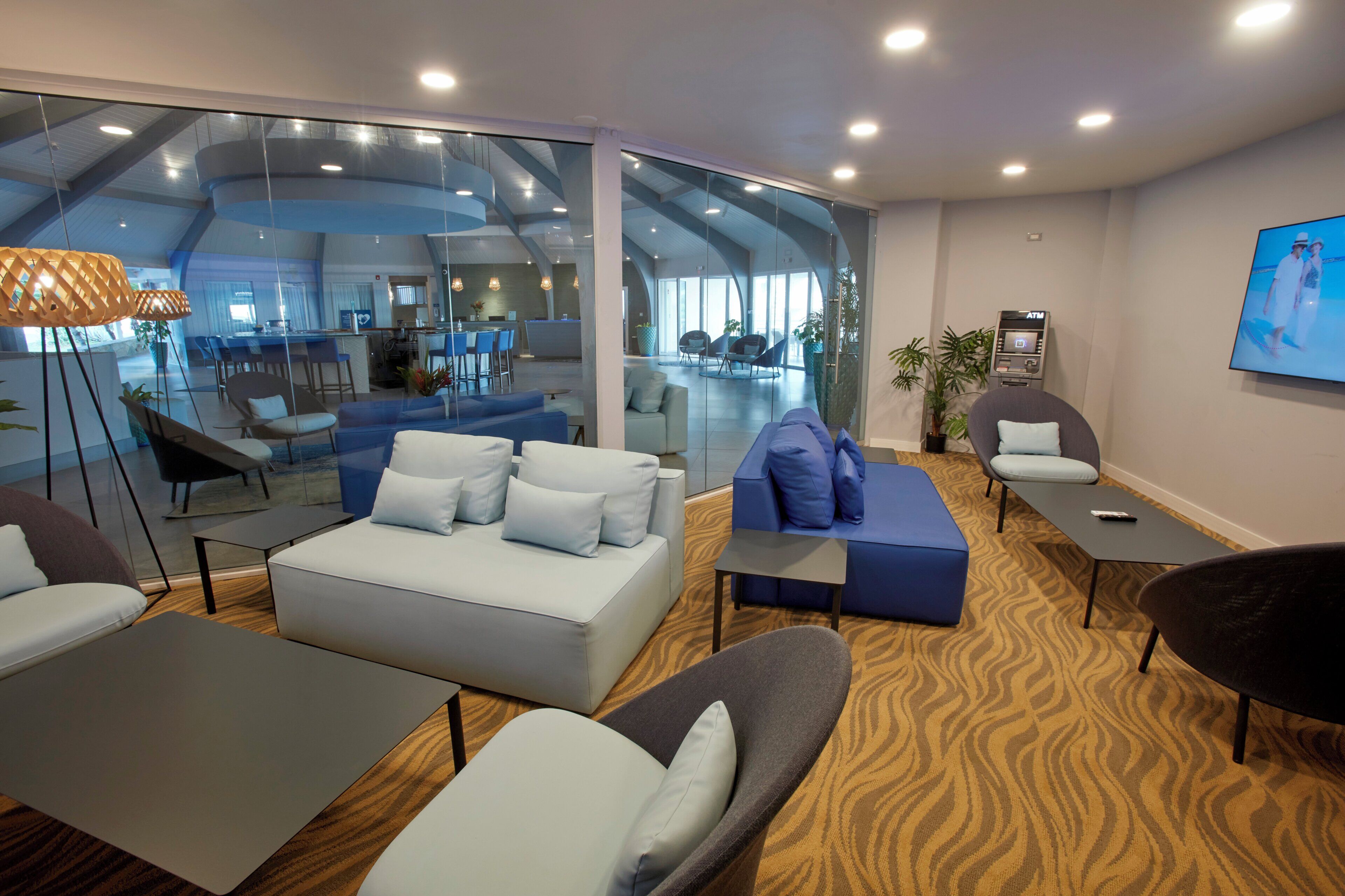 Een moderne hotellobby met zithoeken, een receptiebalie en een grote glazen wand met uitzicht op het interieur.