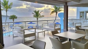 Un restaurante con terraza al aire libre que da al mar, con mesas y sillas blancas, y vistas del océano con palmeras.