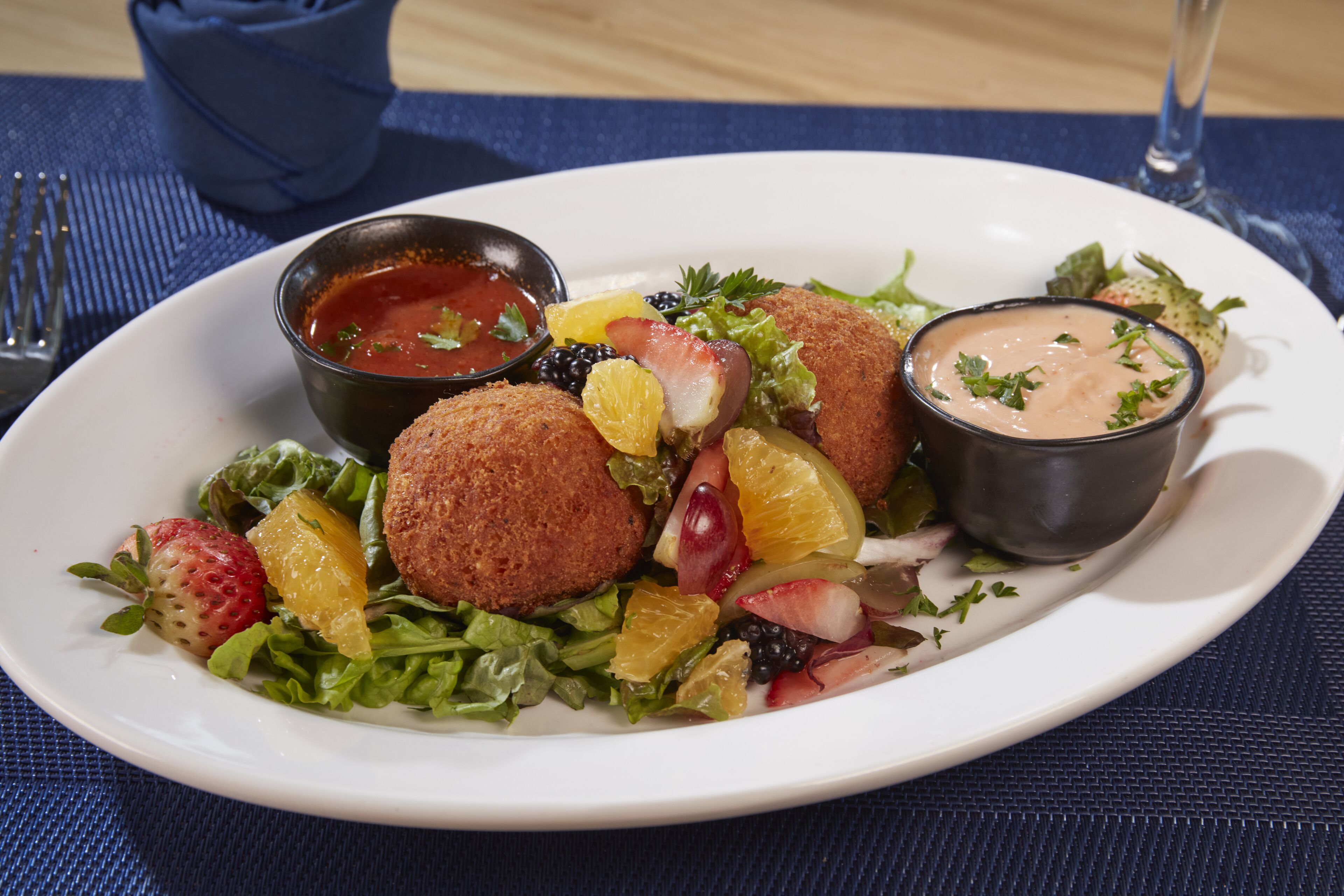 Een bord eten met salade, fruit en twee dipsauzen.