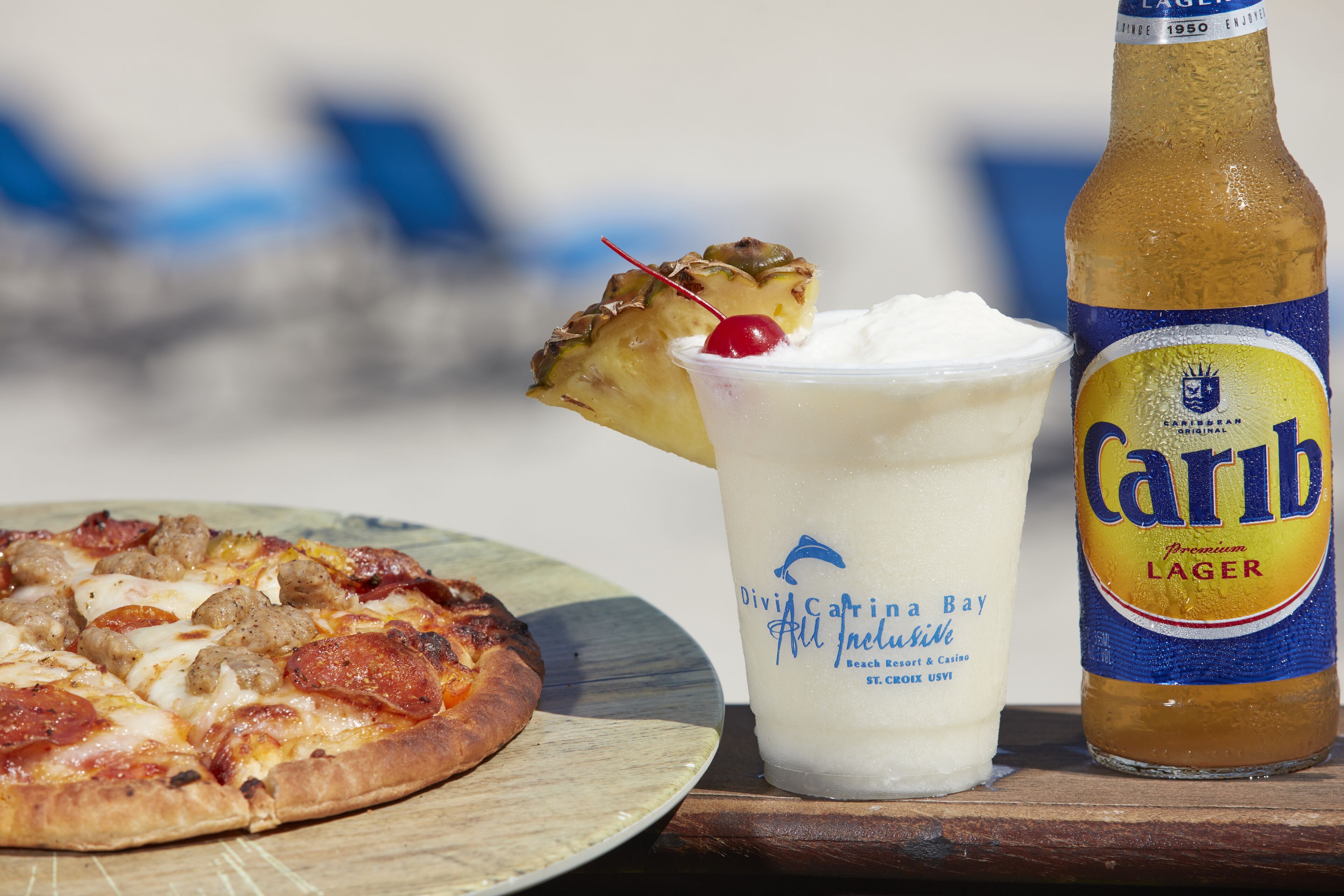 A pizza, a margarita, and a bottle of Carib Lager on a wooden table.