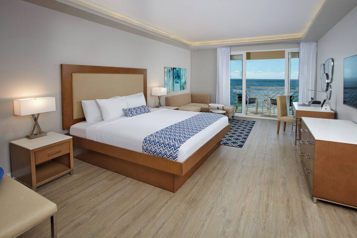 Une chambre d’hôtel moderne avec un grand lit, un bureau, une chaise et une vue sur l’océan.