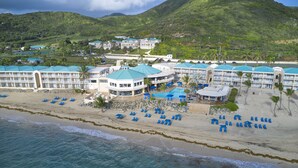 Un hotel frente a la playa con varias construcciones, piscina y tumbonas.