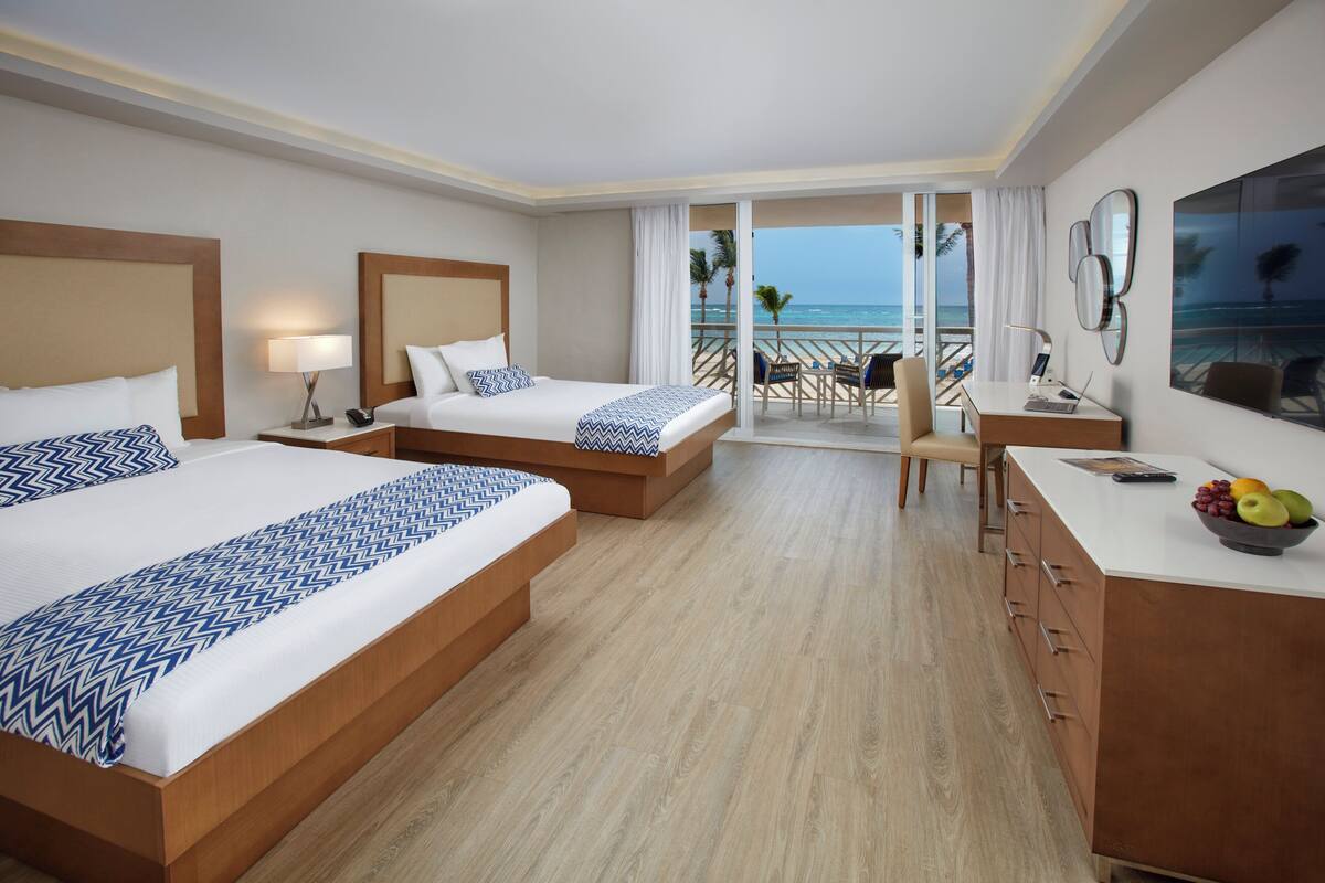 Une chambre d’hôtel avec deux lits, un bureau, une chaise, un ordinateur portable et une vue sur la plage.