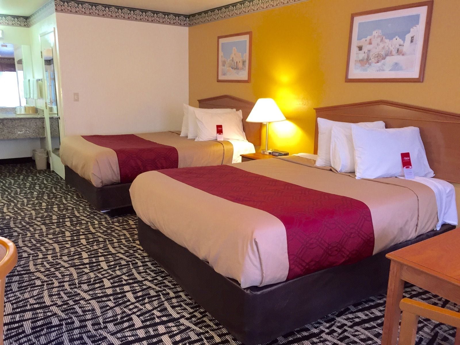 A hotel room with two beds, a small table, a lamp, and a mirror.