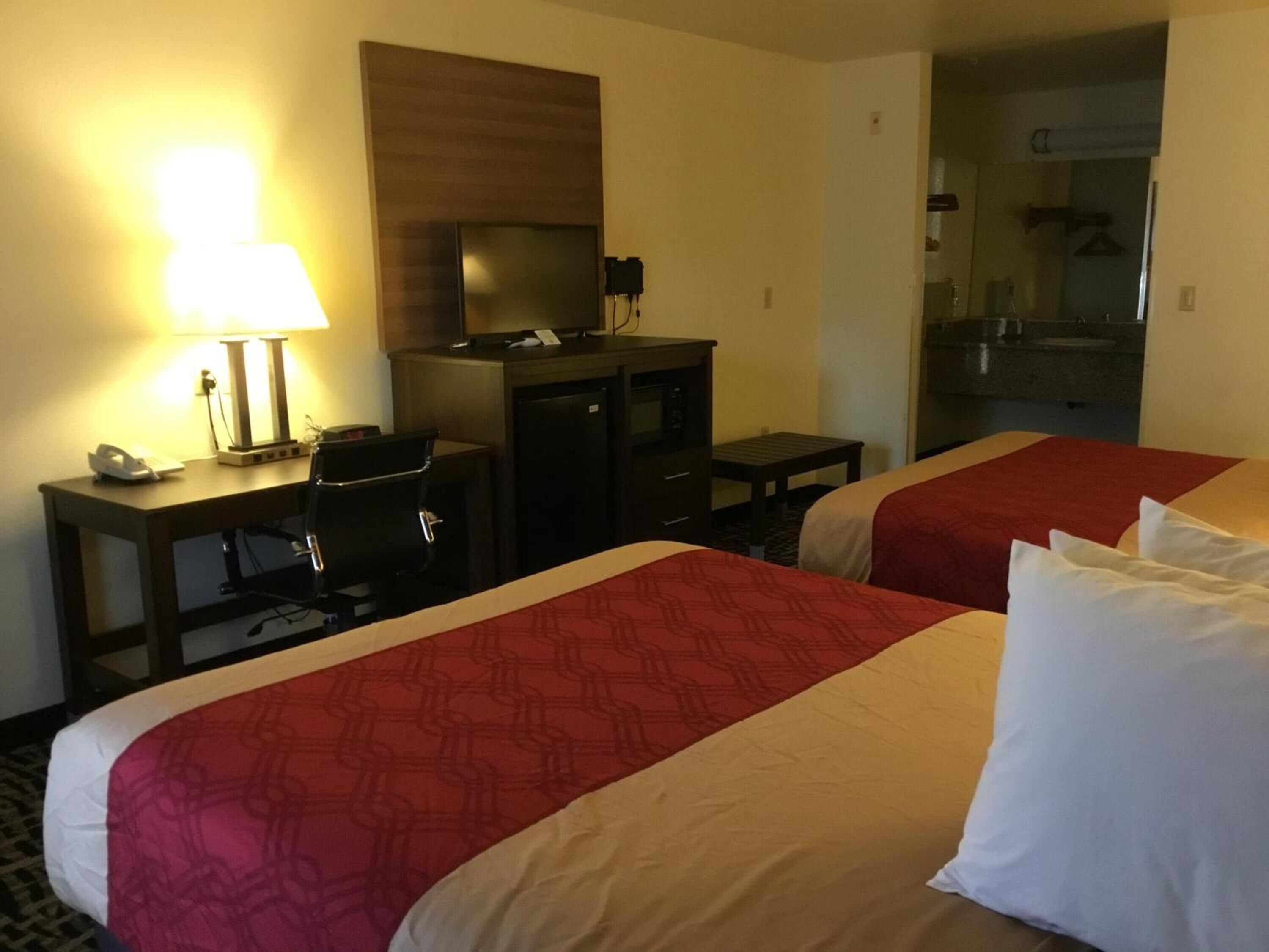 Ein Hotelzimmer mit zwei Betten, einem Schreibtisch mit Computer, einer Lampe und einem kleinen Tisch.
