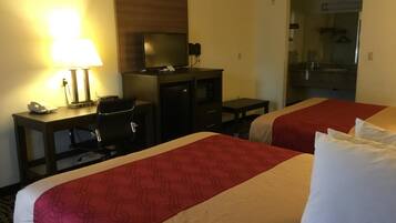 Ein Hotelzimmer mit zwei Betten, einem Schreibtisch mit Computer, einer Lampe und einem kleinen Tisch.