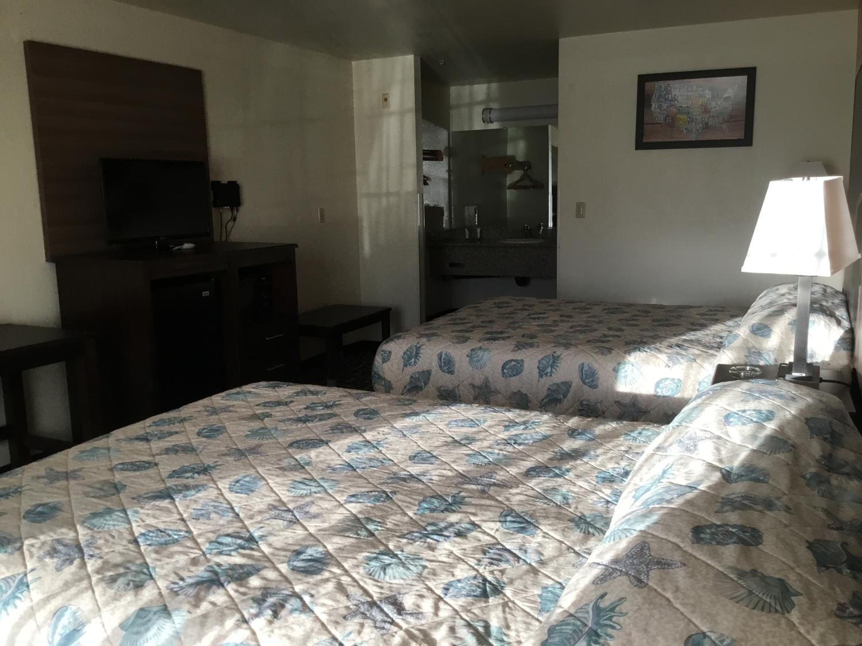 A hotel room with two beds, a desk, a television, a bathroom, and a painting on the wall.