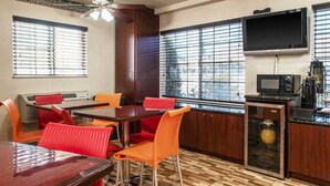 Comedor con una mesa de madera y sillas rojas, ventilador de techo, televisor y cafetera.