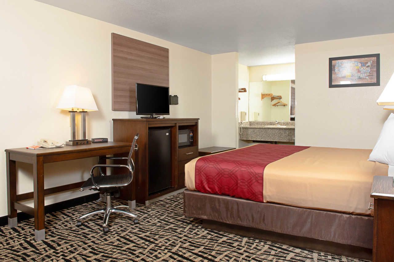 A hotel room with a bed, desk, chair, television, and a bathroom visible in the background.