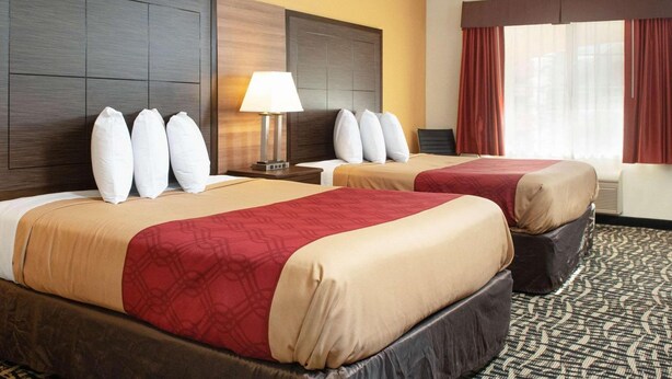 Una habitación de hotel con dos camas, una mesita de noche, una lámpara y un ventanal con cortinas.
