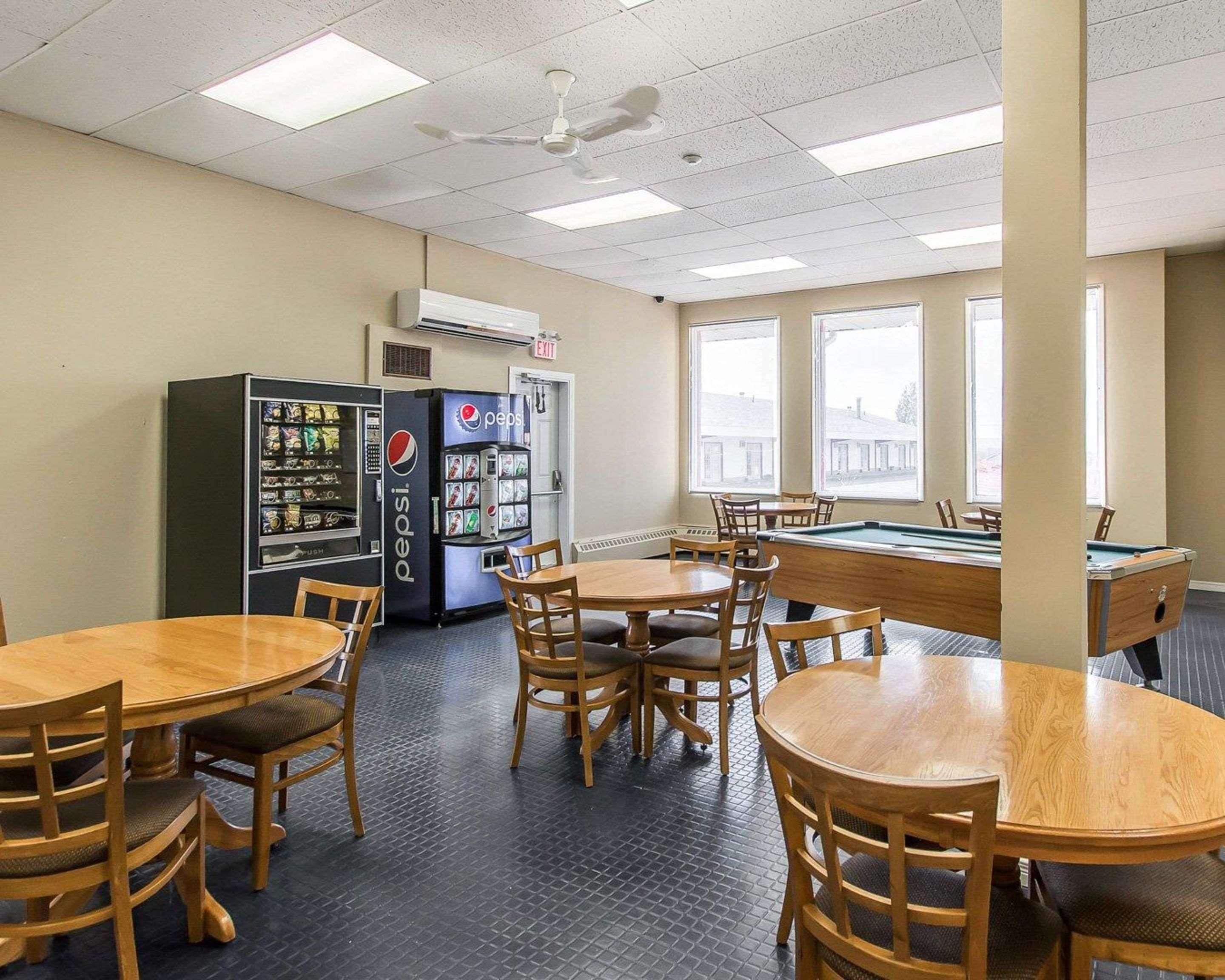 A room with pool tables, chairs, vending machines, and large windows.