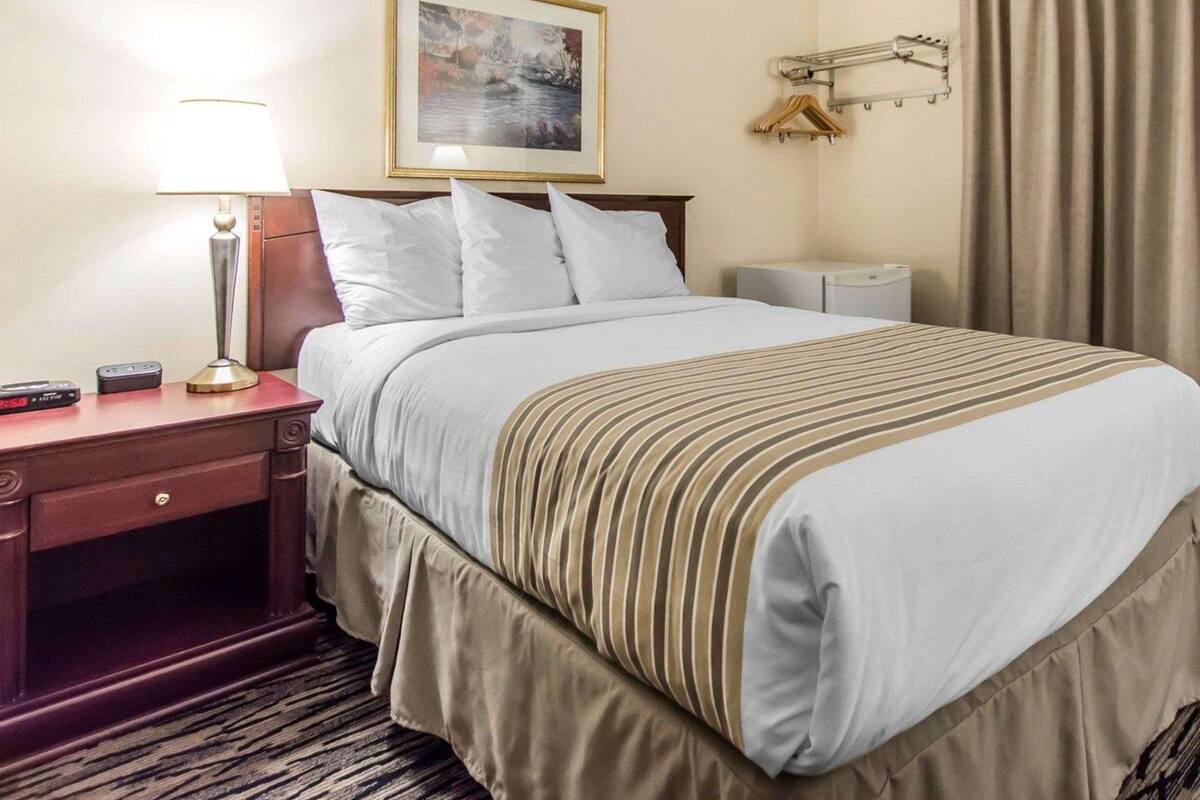 A hotel room with a bed, a nightstand, a lamp, a painting on the wall, and a curtain.