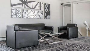 Ein modernes Zimmer mit einem schwarzen Ledersofa, einem Glastisch und abstrakter Wandkunst.