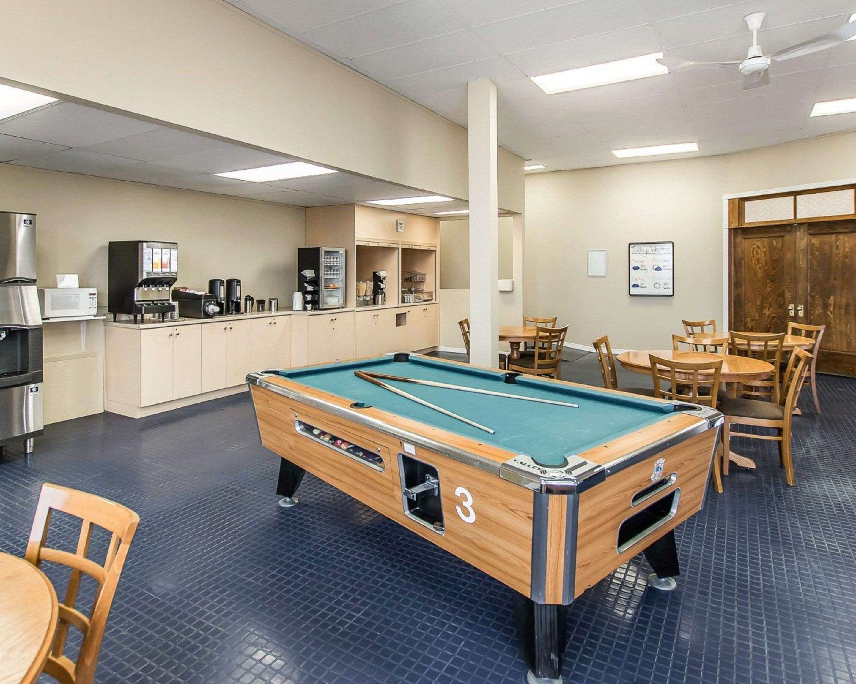A pool table in a room with a kitchenette, tables, and chairs.