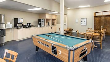 A pool table in a room with a kitchenette, tables, and chairs.